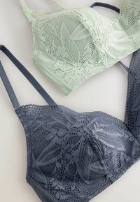 Två spetsbehåar: en mintgrön och en marinblå. De har blommönster, justerbara band och texturerad tyg för en ömtålig look.