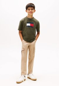 Olivgrön T-shirt med en flerfärgad grafikdesign, tillsammans med beige cargobyxor och vita sneakers med beige accenter.