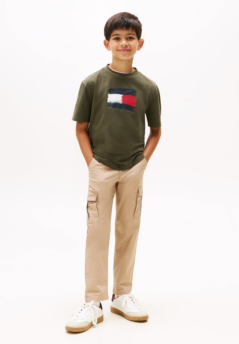 Olivgrön T-shirt med en flerfärgad grafikdesign, tillsammans med beige cargobyxor och vita sneakers med beige accenter.