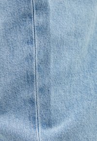 Vaaleansininen farkkukangas, jossa näkyy vino kaltais-kuvio ja korostettu sauman yksityiskohta, sileä tekstuuri ja lievä haalistuma.