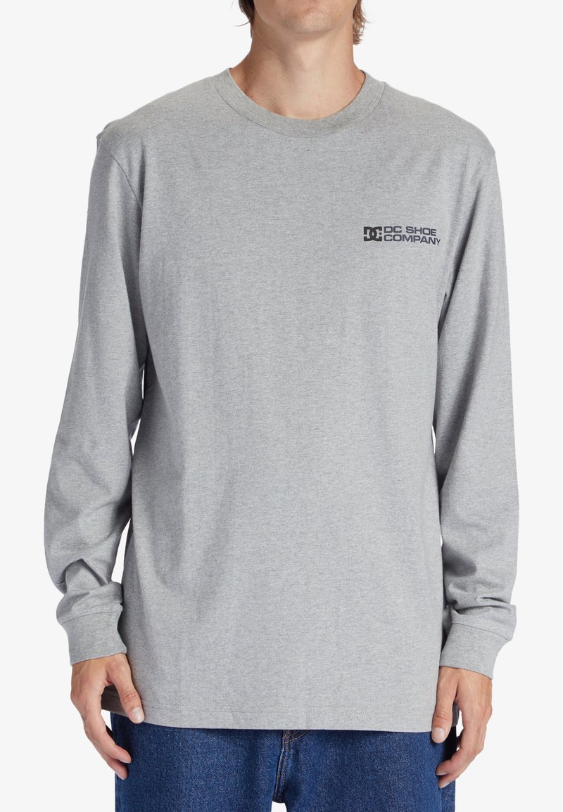 Long-sleeve gray cotton t-shirt featuring a black logo on the upper left chest and a classic crew neckline. Soft texture, relaxed fit.