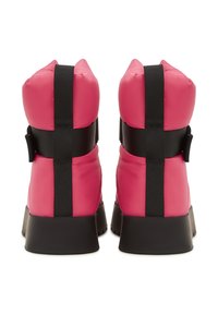 Egy rózsaszín téli csizma pár fekete elasztikus pántokkal és vastag fekete talppal, hátulról nézve, fehér háttér előtt.