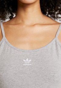 Szary bawełniany top na ramiączkach z okrągłym dekoltem i cienkimi ramiączkami, z małym białym logo Adidas na obszarze klatki piersiowej. Miękka struktura.