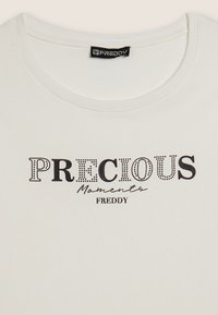 Camiseta de algodón blanca con el texto "Momentos PRECIADOS" en negro con un patrón de puntos y "FREDDY" en una fuente cursiva debajo.