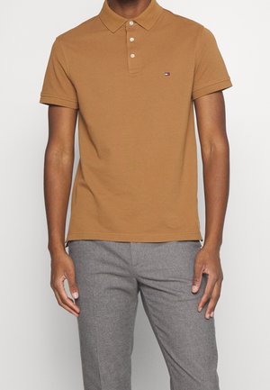 Polo marron avec col, patte de boutonnage à trois boutons et manches courtes. Présente un petit logo sur la poitrine et une texture de tissu lisse.