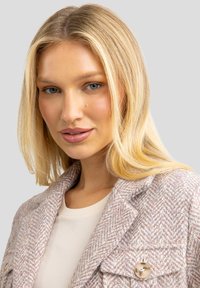 Heled roosa ja kreemi värvi tweed jakk, millel on nurgelised kraed, kaks klappi taskut ja suur nööbi detail. Pehme tekstuur ja struktureeritud kuju.