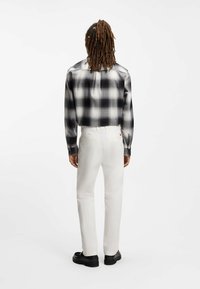 Άσπρο παντελόνι με ίσια μπατζάκια και τσέπες, συνδυασμένο με πουκάμισο σε ασπρόμαυρο καρό σχέδιο. Το πουκάμισο έχει μακριά μανίκια και άνετη εφαρμογή.