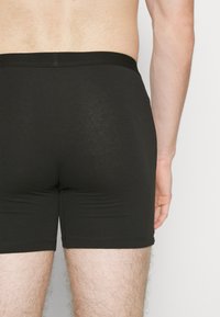 Black cotton boxer shorts with a snug fit, featuring a smooth waistband and contrasting stitching. Texture appears soft and minimal.