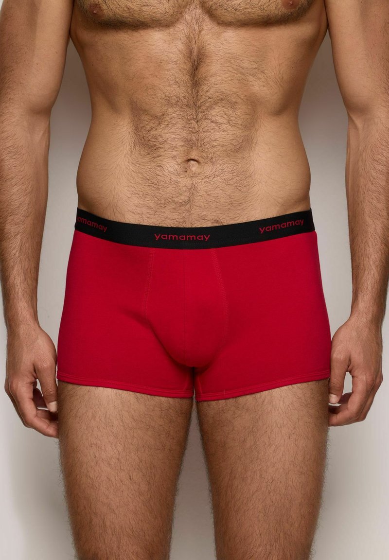 Calzoncillos boxer rojos de tela suave con una cinturilla negra que presenta el logo "yamamay". El diseño se ajusta cómodamente con un espacio definido para la bolsa.