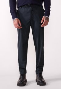 Pantalons vert foncé avec une taille élastique, poches latérales et une coupe droite, associés à des bottes noires à lacets.