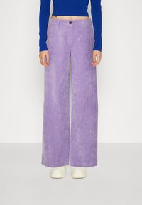 Vida bredbenta kordflorbyxor i ljuslila med vertikala ribbor, med en frontknappstängning och matchade med vita sneakers.