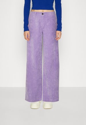 Vida bredbenta kordflorbyxor i ljuslila med vertikala ribbor, med en frontknappstängning och matchade med vita sneakers.