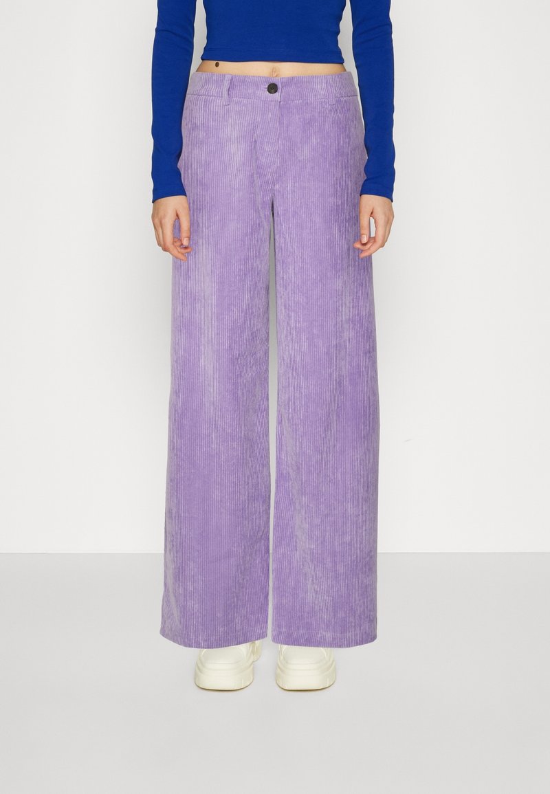 Vida bredbenta kordflorbyxor i ljuslila med vertikala ribbor, med en frontknappstängning och matchade med vita sneakers.