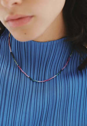 Collar de cuentas multicolores sobre una blusa azul con pliegues. El collar presenta pequeñas cuentas redondas en tonos rosa, verde y negro, creando un diseño delicado.