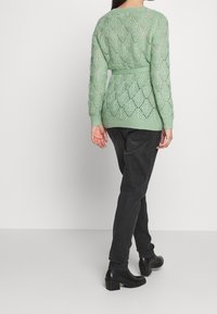 Pull en tricot vert menthe avec un motif en losange, ceinturé à la taille. Stylisé avec un pantalon noir et des bottines. Design texturé et à tissage ouvert.