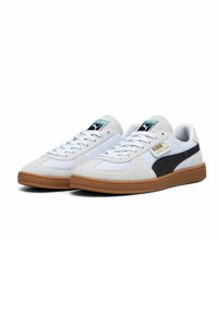 Sneakers bianchi con tomaia in suede, dettagli in rete e una striscia laterale nera. Presentano una suola in gomma naturale e un marchio azzurro chiaro sulla linguetta.