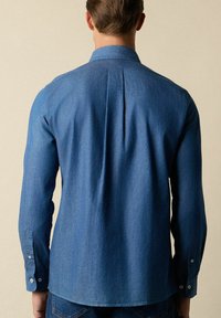 Donkerblauwe denim shirt met lange mouwen, knoopmanchetten en een rugplooi. Heeft een klassieke kraag en een gladde, textuurachtige stof.