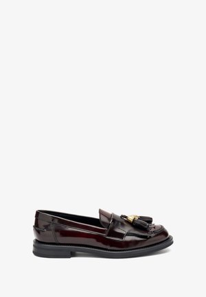 Mocassin en cuir brun foncé poli avec semelle noire, pampilles décoratives et accent métallique doré à l'avant.