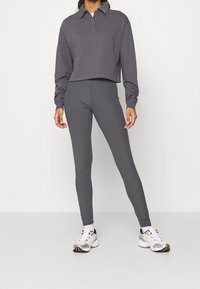 Szara krótka bluzka z długim rękawem, z kołnierzykiem i detalami z guzikami, w połączeniu z pasującymi szarymi legginsami i białymi sportowymi butami z akcentami.