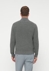 Γκρίζα, ριγέ πλεκτή μπλούζα με ψηλό γιακά και μακριά μανίκια. Διαθέτει καθαρό φινίρισμα και εφαρμοστό τελείωμα. Η υφή φαίνεται μαλακή και ζεστή.