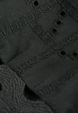 Tessuto nero che mostra un ricamo intricato con accenti testurizzati, caratterizzato da motivi e piccole aperture in tutto il materiale.