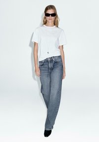T-shirt bianca in cotone, jeans in denim grigio chiaro a gamba larga, occhiali da sole neri e tacchi a punta neri. Design semplice con dettagli minimi.