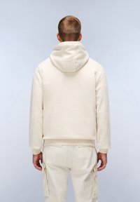 Felpa con cappuccio beige dal tessuto morbido, dotata di tasca a marsupio e polsini a costine, indossata con pantaloni cargo beige abbinati.