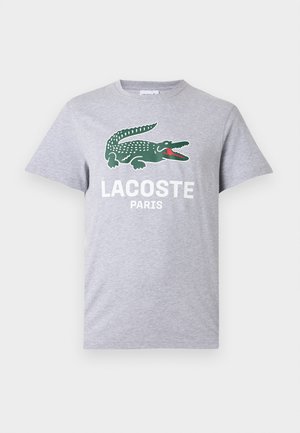 Jasnoszary t-shirt z krótkim rękawem z zielonym logo krokodyla i białym napisem "LACOSTE PARIS" na środku klatki piersiowej.