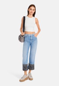 White sleeveless cropped top, light blue straight-leg jeans with leopard print cuffs, and beige platform sneakers. Black leopard print handbag.