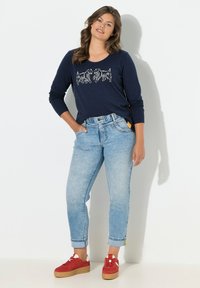 Maglietta a maniche lunghe blu navy con grafica bianca di un animale, jeans azzurri con risvolto e sneakers rosse con dettagli bianchi. Materiale in morbido cotone.