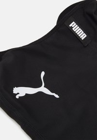 Svart treningstop laget av teksturert stoff, med en hvit Puma-logo på venstre side og et svart merke med logo på skuldersømmen.