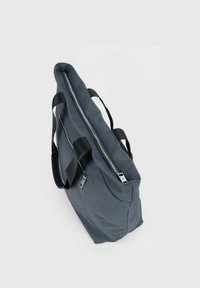 Sac fourre-tout gris en tissu doux, doté de deux poignées noires et d'une fermeture éclair argentée sur le dessus. Design épuré et rectangulaire.