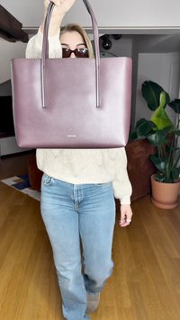 Sac fourre-tout bordeaux avec une texture lisse, un design épuré, des poignées noires doubles et un logo embossé à l'avant. Présenté dans un intérieur de maison.