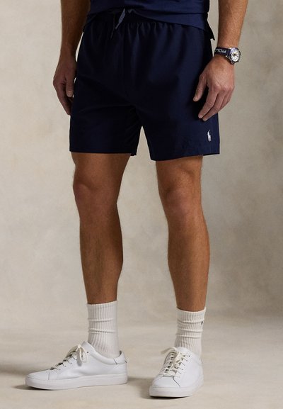 Tamsiai mėlyni plaukimo šortai iš lengvos medžiagos, su elastiniu juosmeniu ir raišteliais. Mažas logotipas kairėje pusėje. Derinami su baltais sportbačiais.