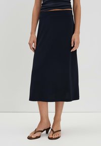 Jupe midi bleu marine en tissu doux, avec une taille lisse et un ourlet évasé. Associée à des sandales à talons striées marron.