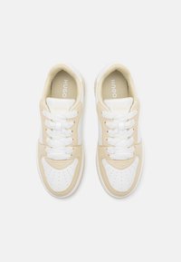Beige and white sneakers with a smooth leather finish, round toe, perforated design, and flat white laces. Gold branding on tongue.