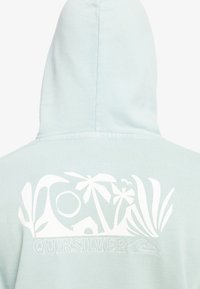 Light blue hooded sweatshirt featuring a white graphic design of palm trees, a house, and waves, with "QUIKSILVER" text below.