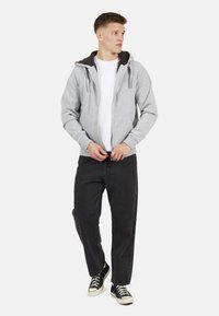 Grijze zip-up hoodie met een donkere binnenvoering, voorkanten met zakken en trekkoorden; gecombineerd met zwarte broek en zwarte high-top sneakers.