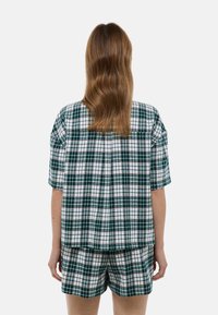 Ensemble de haut à manches courtes en tissu à carreaux et short en vert, blanc et rouge. Le tissu est léger avec une coupe décontractée et un détail de plissage à l'arrière.