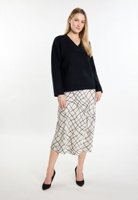 Czarny dziergany sweter z dekoltem w serek, zestawiony z kremową spódnicą w czarny wzór kratki. Modelka nosi czarne szpice.