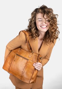 Bolso de piel marrón claro con forma estructurada, que presenta un bolsillo frontal con cremallera y herrajes en tono dorado. Acabado texturizado y asas resistentes.