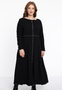 Schwarzes Langarmkleid aus strukturiertem Stoff mit einem gewellten Saum und Bündchen sowie weißen Nähdetails, die das Oberteil teilen.