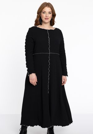 Schwarzes Langarmkleid aus strukturiertem Stoff mit einem gewellten Saum und Bündchen sowie weißen Nähdetails, die das Oberteil teilen.