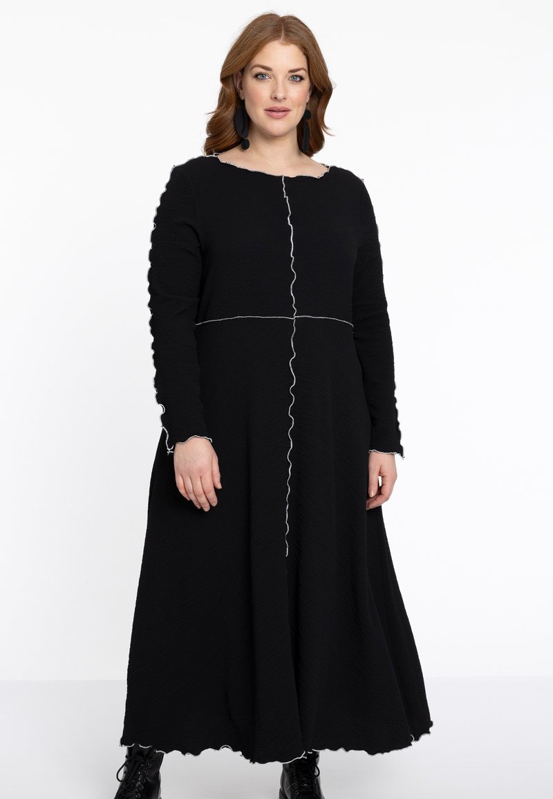 Schwarzes Langarmkleid aus strukturiertem Stoff mit einem gewellten Saum und Bündchen sowie weißen Nähdetails, die das Oberteil teilen.