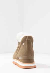 Bottine en suede marron avec un col en fausse fourrure blanche, semelle en caoutchouc texturée, et couches orange et blanche contrastées sur la semelle.