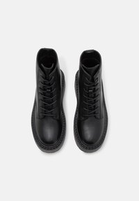 Černé kožené kotníkové boty s hladkou texturou, se šněrováním vpředu a robustní podrážkou s kontrastním prošíváním.