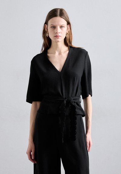 Haut noir à manches courtes avec un col en V, en tissu texturé, et une ceinture nouée à la taille avec des bords festonnés. Design simple et moderne.