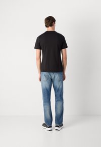 Tricou negru din bumbac cu mâneci scurte, combinat cu blugi denim de un albastru deschis. Ținuta este completată cu adidași negri și albi.