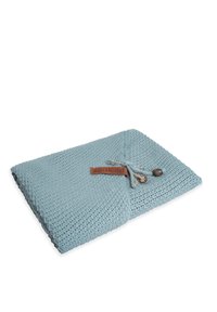 Coperta lavorata a maglia di un blu chiaro con un motivo testurizzato, dotata di un'etichetta in pelle marrone e decorazioni grigie e in legno.