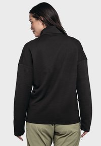 Schwarzer, gerippter Pullover mit hohem Kragen, langen Ärmeln und lockerer Passform. Der Stoff hat eine strukturierte Optik.